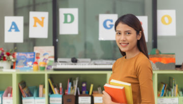 Professora na escola segurando livros.