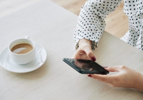 Coordenadora pedagógica lendo novidades de educação no celular e tomando café