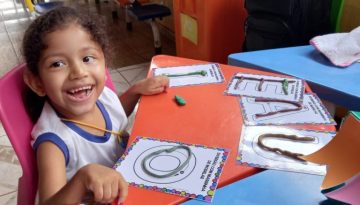 Criança sorrindo com mãos apoiadas em mesa escola durante uma educação inclusiva