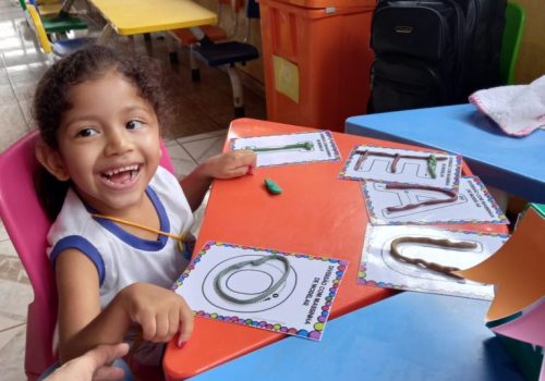 Criança sorrindo com mãos apoiadas em mesa escola durante uma educação inclusiva