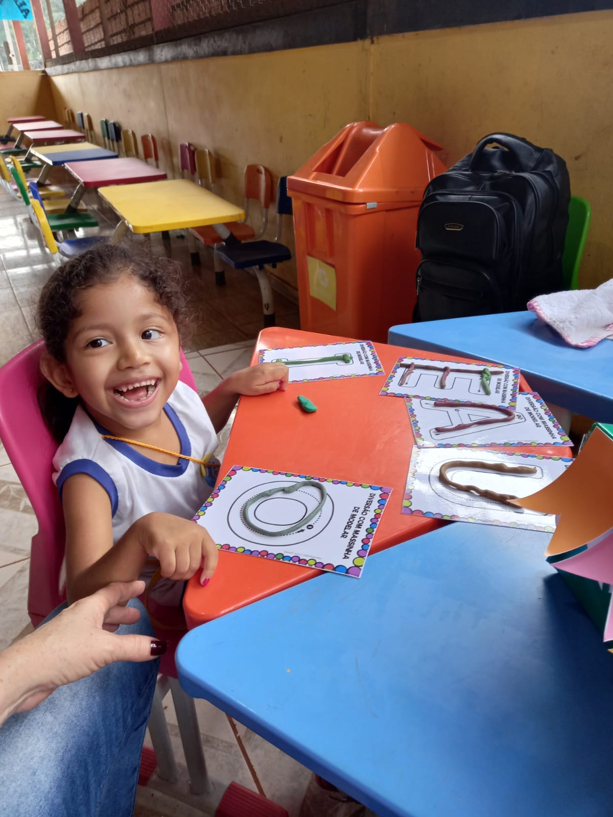 Criança sorrindo com mãos apoiadas em mesa escola durante uma educação inclusiva