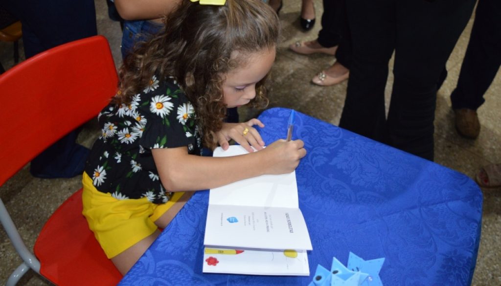 Menina autografando o próprio livro em evento de incentivo à evolução dos crianças.