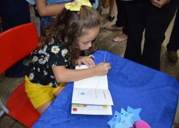 Menina autografando o próprio livro em evento de incentivo à evolução dos crianças.