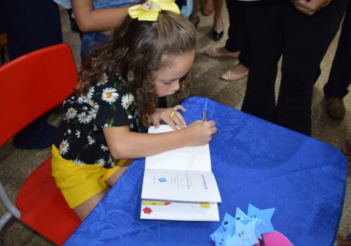 Menina autografando o próprio livro em evento de incentivo à evolução dos crianças.