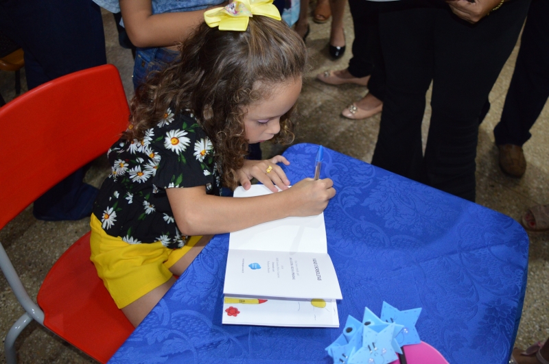 Menina autografando o próprio livro em evento de incentivo à evolução dos crianças.