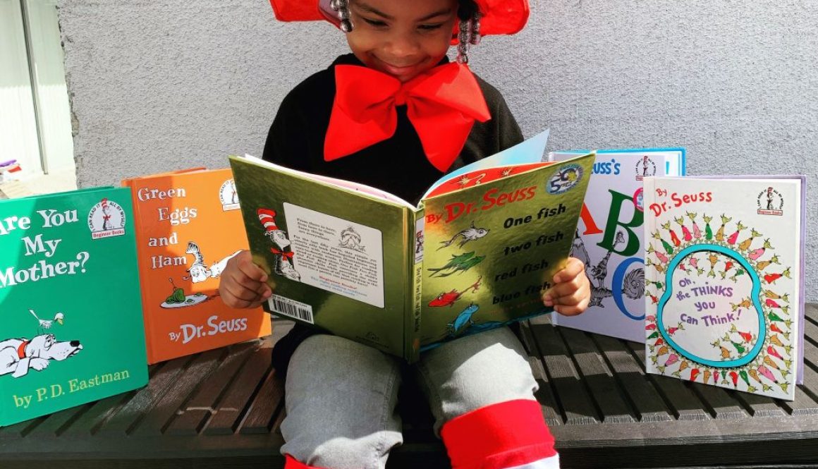 Menina de etnia negra, aparentando ter 3/4 anos de idade, com um chapéu grande, listrado de vermelho e branco sobre sua cabeça, lendo um livro com título em inglês, chamado: “One fish, two fish, three fish, four fish”, do Dr. Seuss, para mostrar os efeitos de uma educação antirracista.